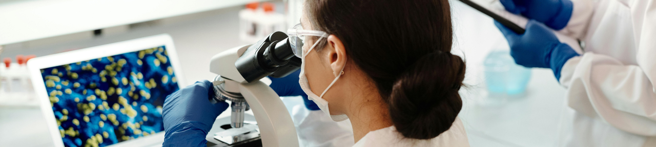 Researcher examines slides under a microscope (c) UC Regents. All rights reserved.