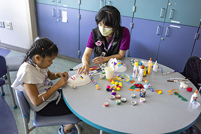 A healthcare worker helping a child patient paint a mask.