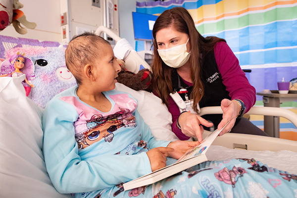 Child life specialist holds book with patient in bed