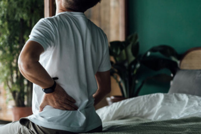 A senior Asian man holds his lower back while seated.