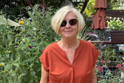 A woman with blonde hair is wearing an orange shirt and sunglasses.