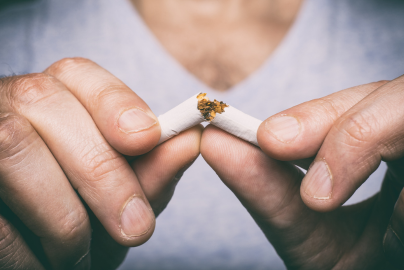 Two hands break a cigarette in half.