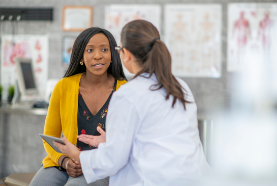 A female patient and female doctor talk in an exam room. 