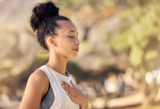 Woman standing outside with her eyes closed and hand on her heart taking care of her mental health.