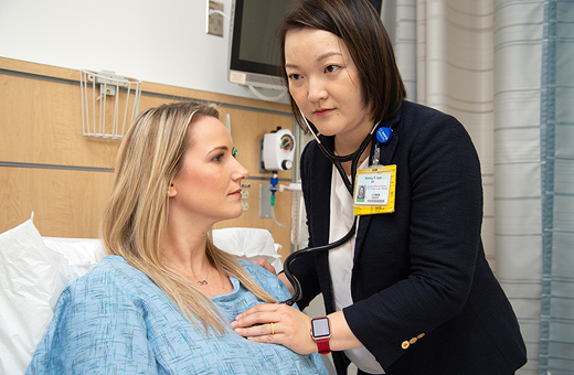 Female physician listening to the heart of a female patient in a hospital bed with a stethoscope