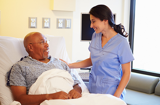 Male patient in hospital bed preparing for pacemaker surgery with health care provider next to him.