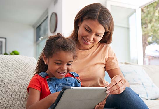mother and daughter on a couch looking at a tablet together