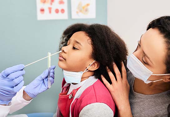 A young girl gets a nasal swab for a COVID-19 test at the doctor&#x2019;s office with her mom. 