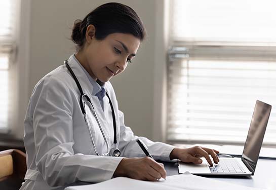 Female doctor sitting in front of a computer and taking notes