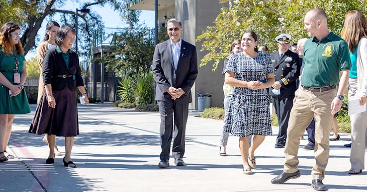 A group of adults walks along a sidewalk next to a school building. 