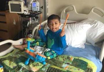 Isaac sitting in a hospital bed using his drum sticks