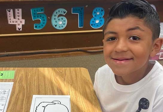 Young male child sitting at a desk in a school room with numbers on the wall