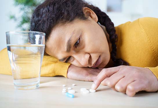 Sad woman looking at prescription pills next to a glass full of water. 