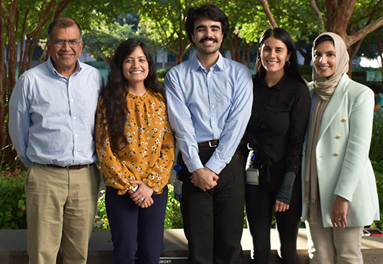 Two professors on left, flanked by three medical students stand outside the Education Building with trees in background
