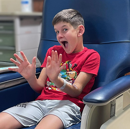 Adam Olson in a treatment room sitting in a blue chair giving a thumbs up