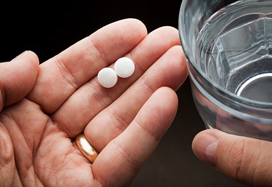 Hand holding two pills and a glass of water