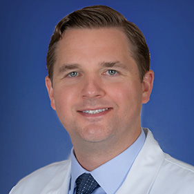 Portrait of head and shoulders of man in white coat.