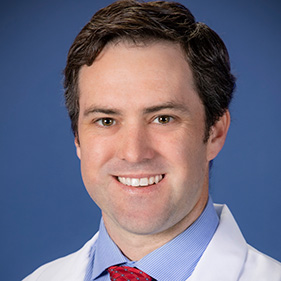 Portrait of head and shoulders of man in white coat.