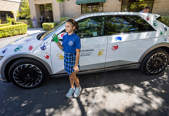 Young female with a green painted hand standing next to a car with handprints