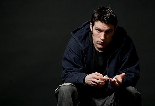 A serious looking young man stares at the camera while holding an open bottle of prescription medication