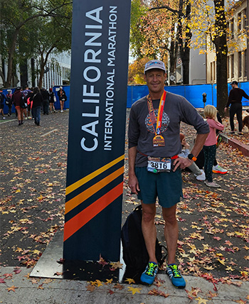 Man wearing medal around neck standing in the street next to sign that says California International Marathon