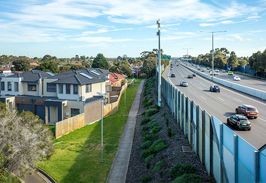 Houses in neighborhood within 50 feet of large freeway with cars driving on it.