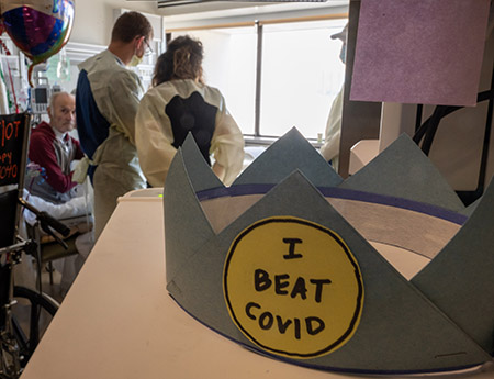 A paper crown that reads "I beat COVID" sits on a table in a hospital room.