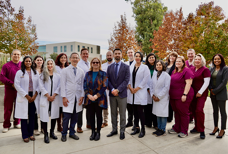 A group of medical professionals wearing scrubs, white coats and business attire gather in a courtyard.