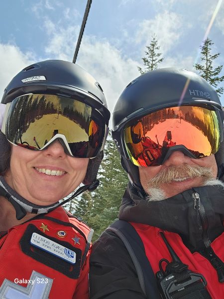 Man and woman with goggles and helmets and snow in background.