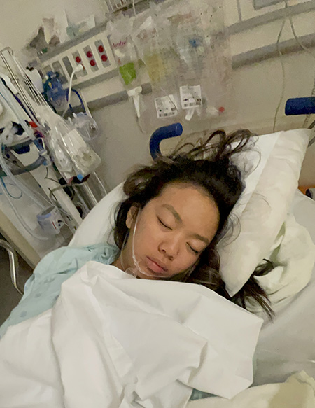 woman lying in hospital bed covered by a sheet.