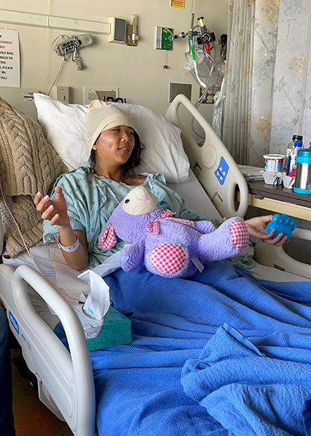 Woman in a hospital bed with a purple stuffed animal nearby
