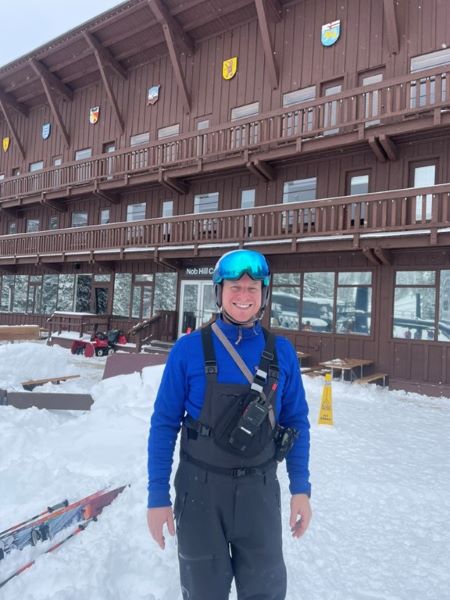 Man in blue ski attire standing in front of lodge.