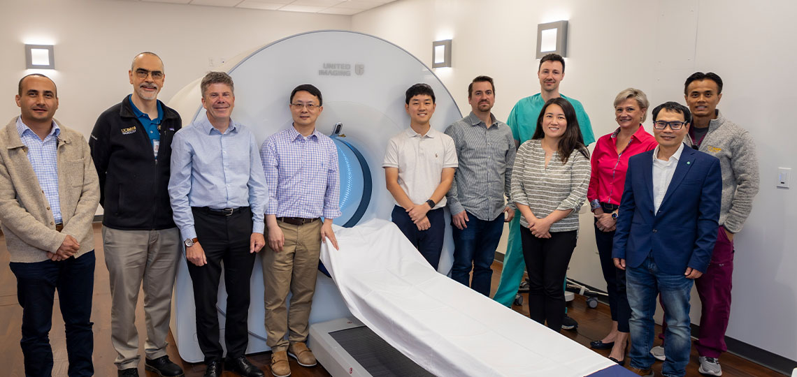 Group of people standing in front of a large PET scanner.