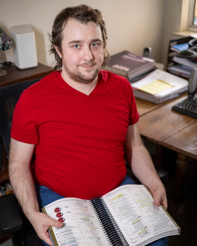 Sean Mini sitting in chair and holding a coding book. 
