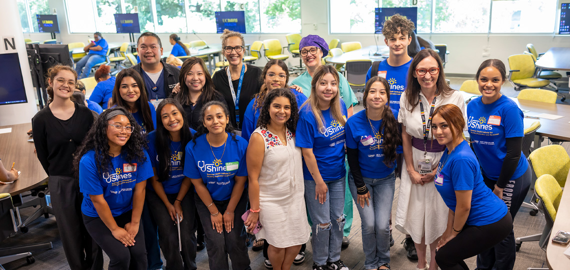 Students wearing blue SHINES shirts stand side-by-side with professors in classroom