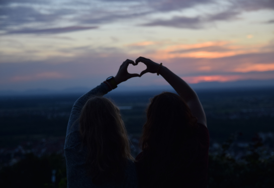Two women form a heart shape with their hands together