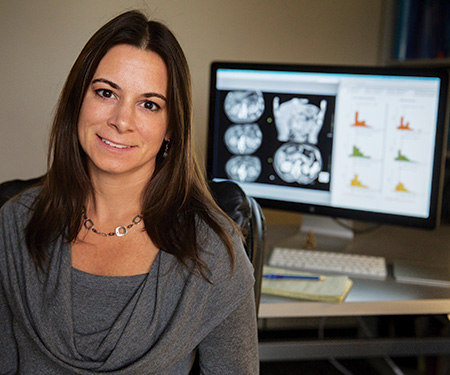 Woman with light brown hair and dark shirt sitting in front of a mammography image.