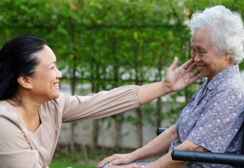 A caretaker smiles at a happy-looking elderly woman in a wheelchair