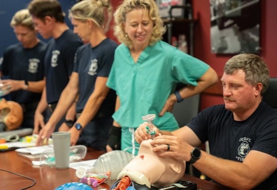 Nurse anesthetist helps firefighters learn how to insert airway device on mannequins. 
