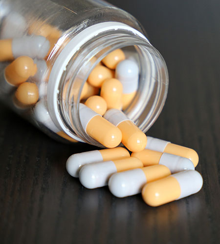 A medicine bottle lays on its side, as yellow and white pill capsules spill out.