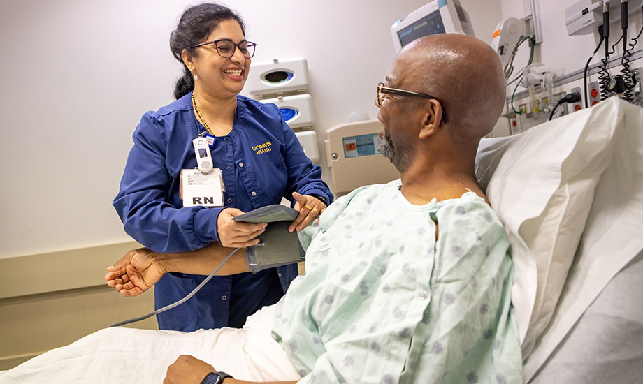 A nurse in blue scrubs stands over a patient in a hospital bed