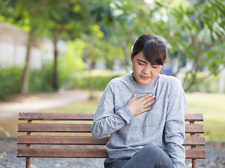 woman holding her chest on a park bench