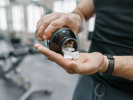 man pouring out bottle of athletic supplement pills