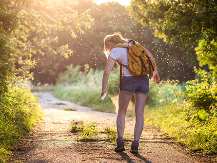 woman spraying mosquito repellent while walking on trail