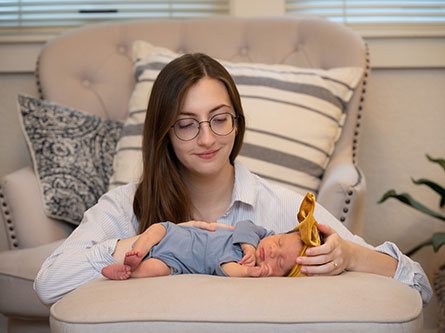 mom looking down with her arms around her infant who is laying down