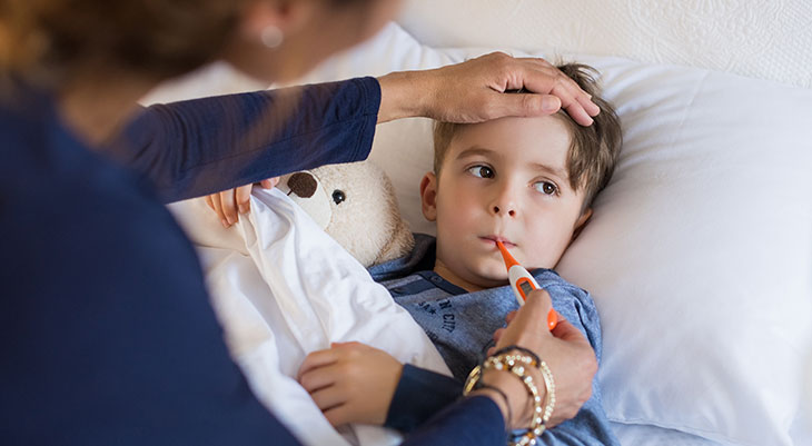 Boy laying in bed getting his temperature taken by his mom