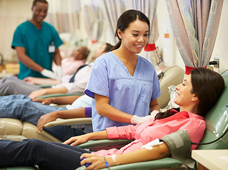 female health care provider drawing blood from donor, with others in the backgrounds