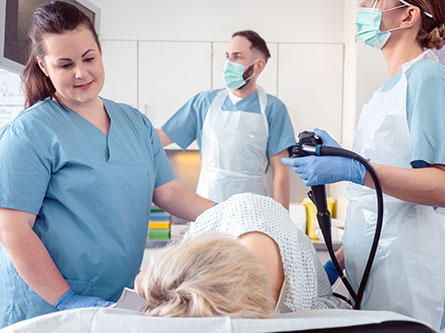 Three health care providers performing colonoscopy on woman laying on a table