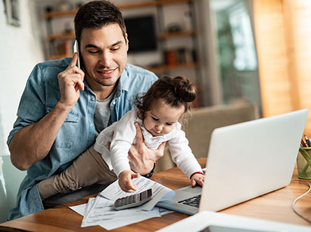 dad holding baby while on a phone call and trying to work on his laptop