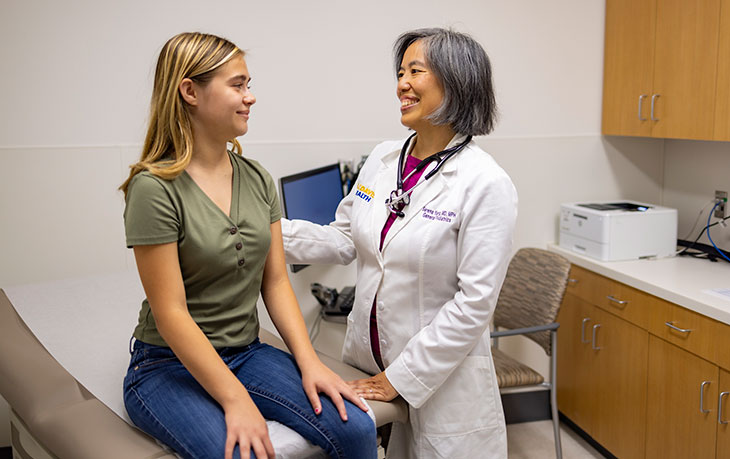 teenage girl sitting on a clinic table in a room with a female health care provider